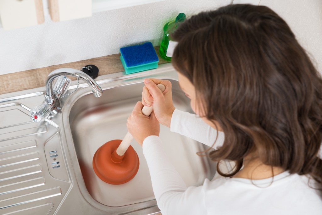 Woman using a plunger in the sink