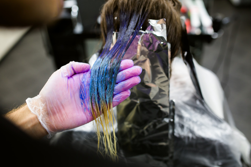 A stylist dying the hair of a cluent blue