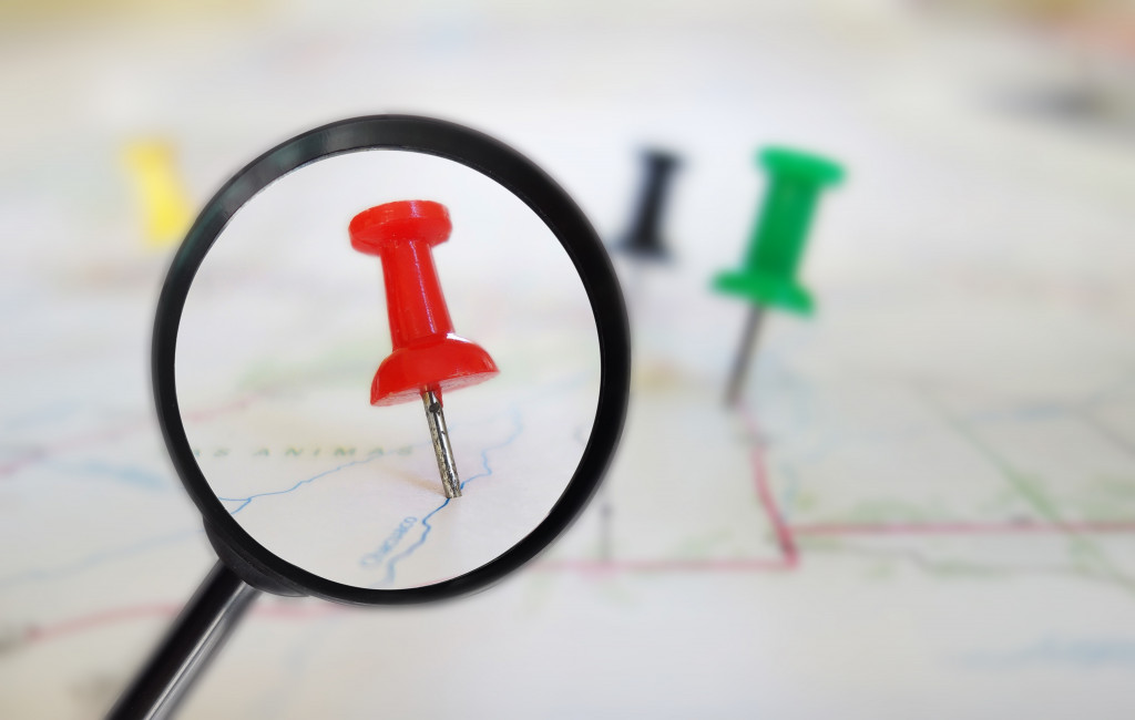 A magnifying glass surveying a red pin among others on a road map