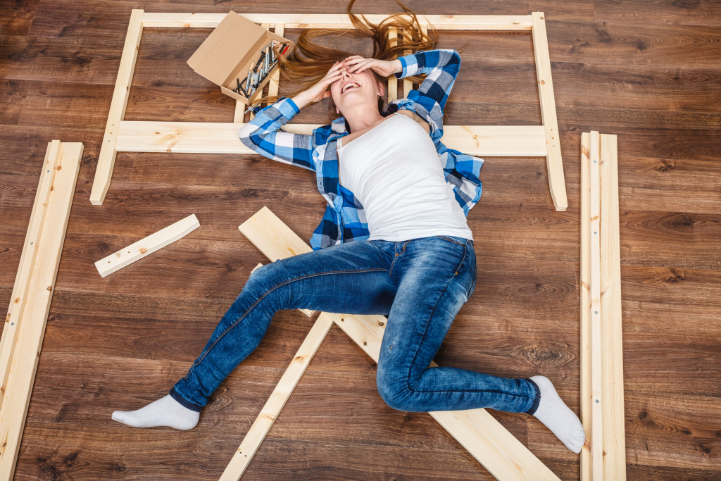 a stressed woman lying in the middle of scattered DIY furniture pieces