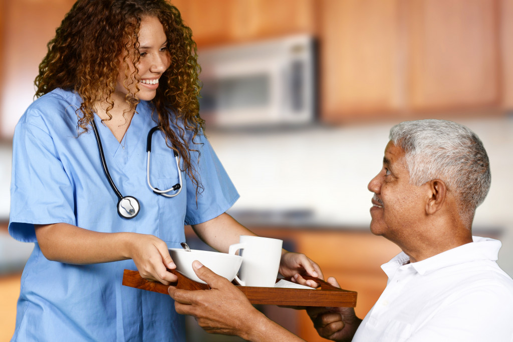 a nurse handing a meal tray to an older male patient